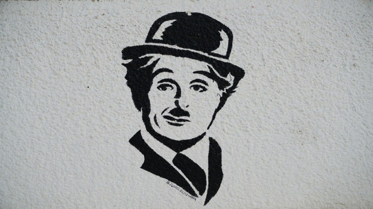 A black and white mural depicting the face of a man in a bowler hat and suit, resembling a classic silent film character.