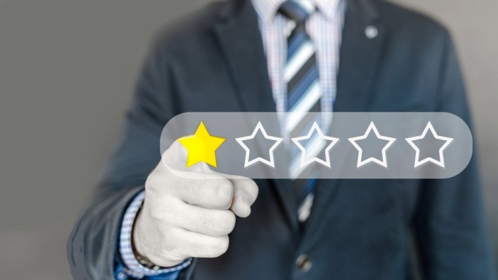 A businessman in a suit holding a hand out to select a one-star rating on a digital feedback interface.