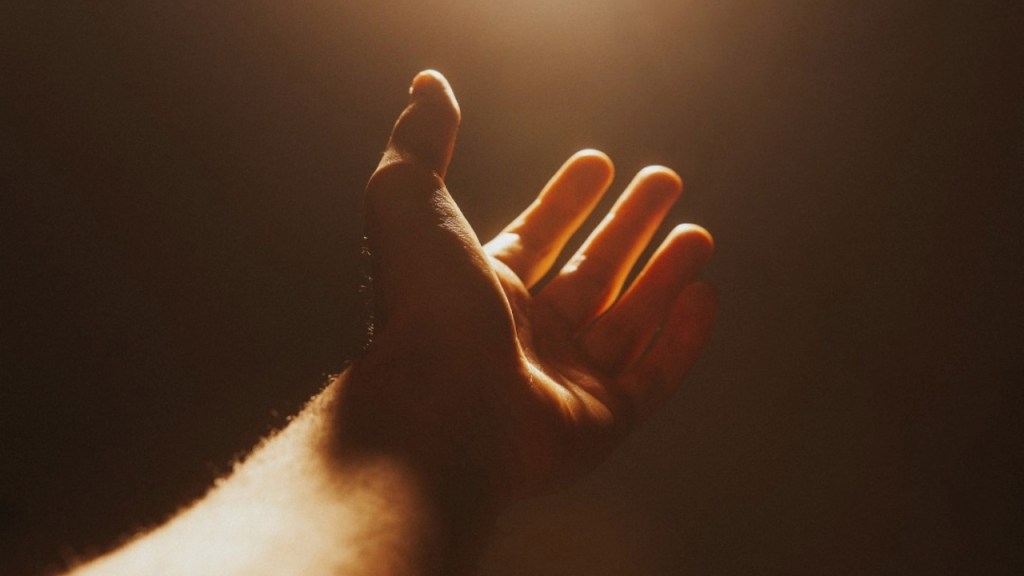 Close-up of an outstretched hand reaching towards a light source, against a dark background.