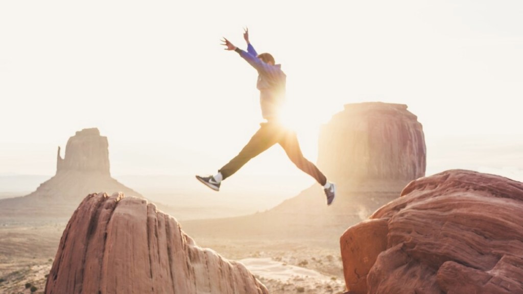 A person jumping between rock formations during sunset in a desert landscape.