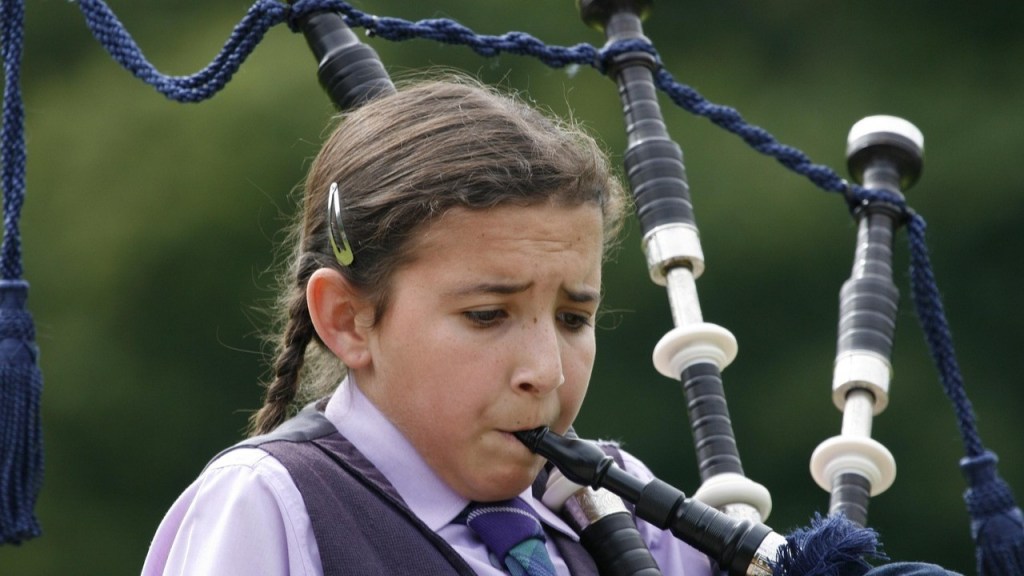 A young person playing a bagpipe, concentrating intently while standing outdoors.