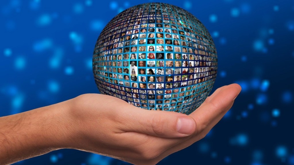 A hand holding a globe made up of numerous images of people's faces, set against a blue background with a bokeh effect.