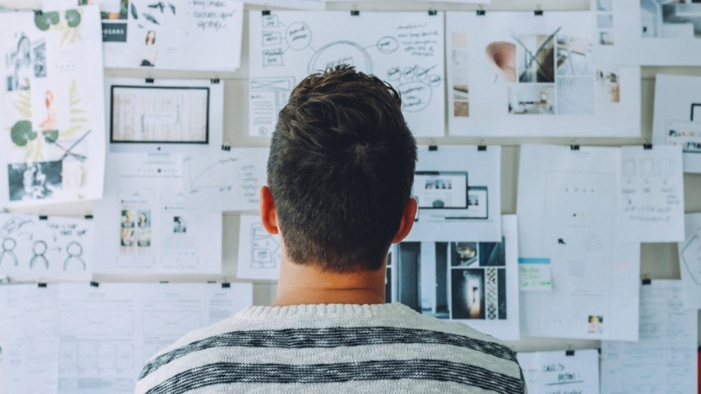 A person standing in front of a wall covered with various papers, notes, and sketches, focusing intently on the material.
