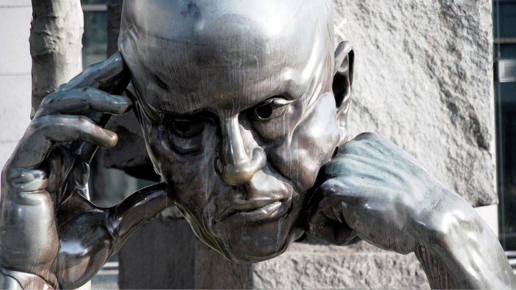Close-up of a bronze sculpture depicting a thoughtful man, resting his head on his hand with a contemplative expression.
