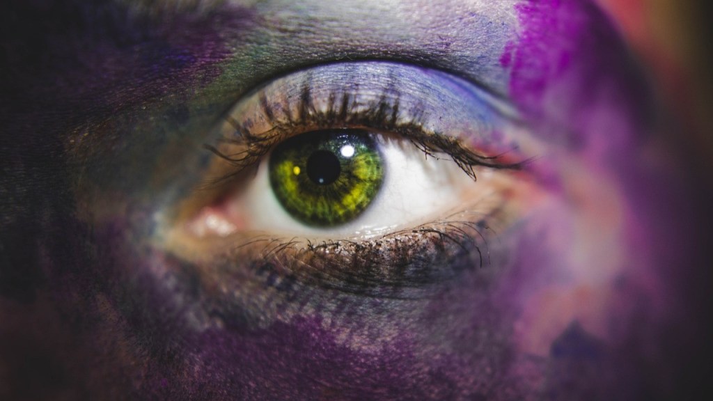 Close-up of a striking green eye with artistic face paint in shades of purple and blue.