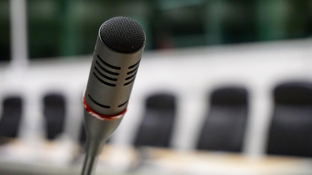 Close-up of a microphone in a meeting room with blurred empty chairs in the background.